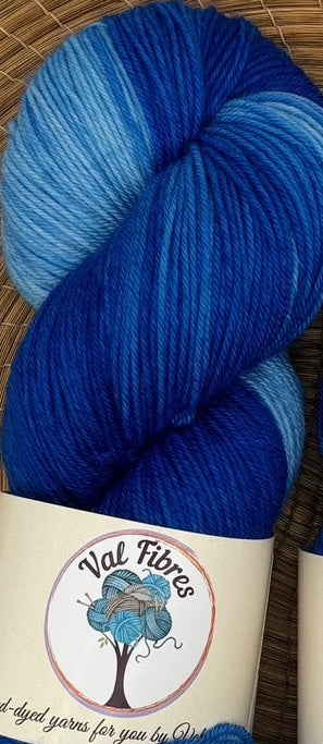 Two blue skeins of yarn with labels on a woven mat